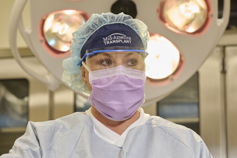 A nurse in scrubs and a visor looks to her left.
