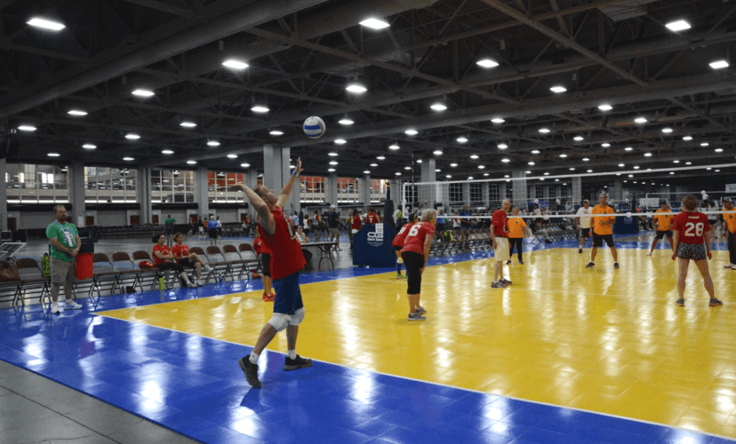 A man in a red shirt abut to spike a volleyball at an indoor court