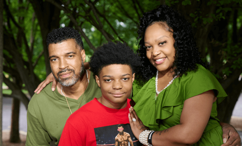 Dee is posed with her husband, Robert Jr. Both of them are wearing green. Their son, Robert III, sits between them in a bright red shirt.