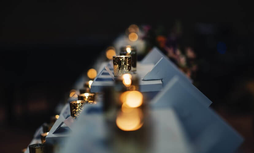 A line of candles glowing forward to back. Only a candle in the middle is in focus.