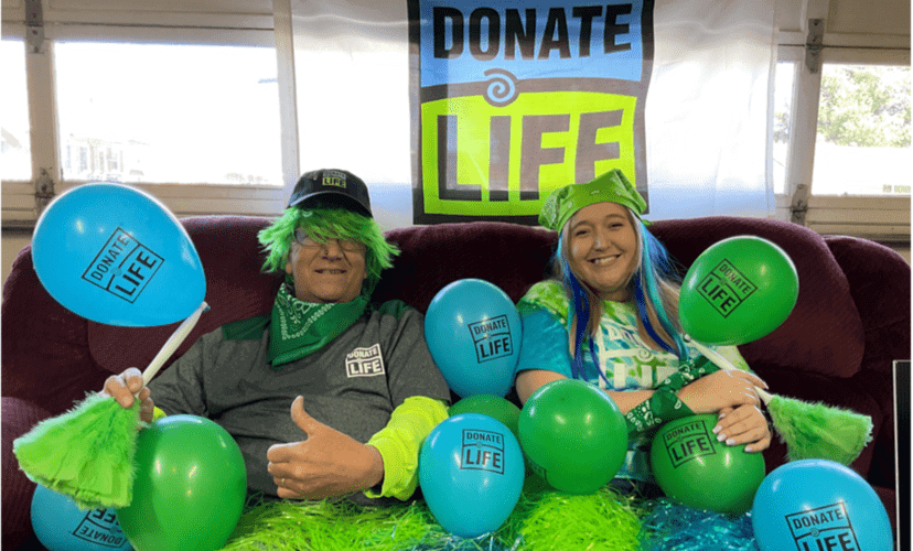 A family celebrating blue and green day. They have a Donate Life flag behind them and are covered in green and blue Donate Life balloons.