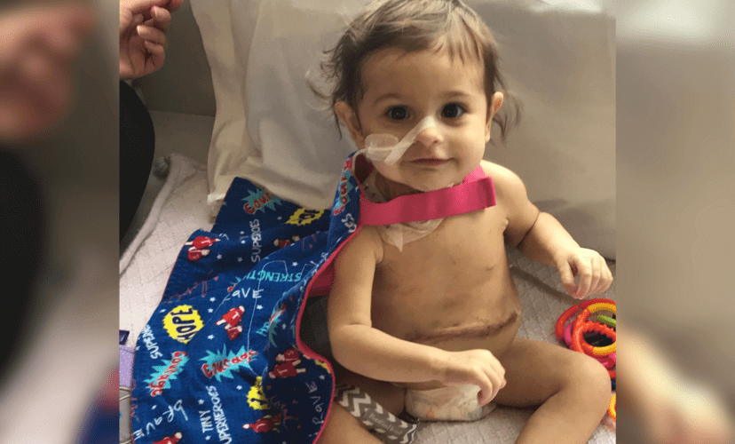 Baby Olivia sitting next to a blue blanket. She has a tube in her nose and a transplant scar on her abdomen.