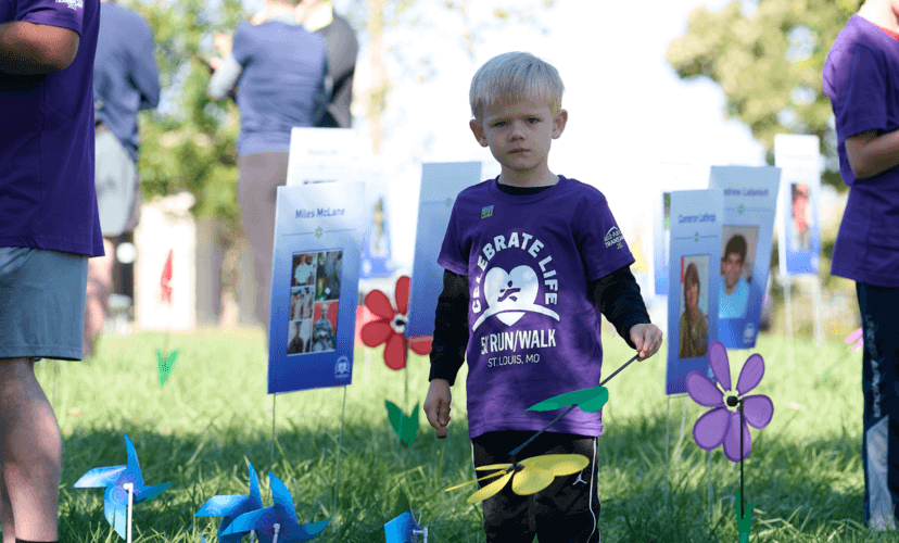 A little boy with blonde hair gazes at the camera. He is standing in the Garden of Heroes at the 2022 Celebrate Life 5k.