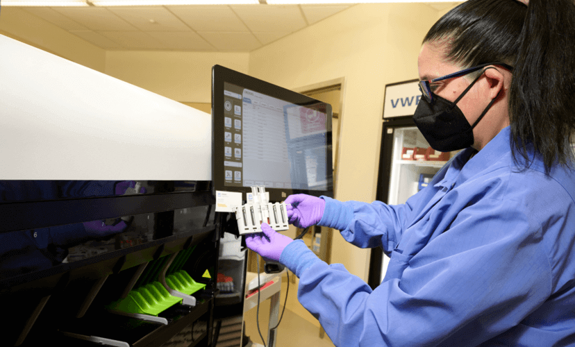 Jennifer M. working in the lab at Mid-America Transplant. She is wearing purple gloves and a black face mask.