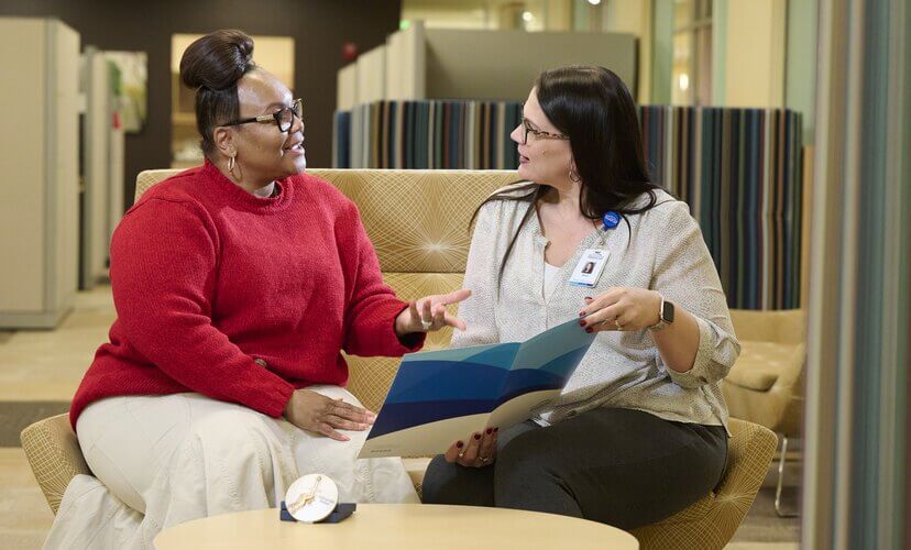 Two women discussing the donation process. A Mid-America Transplant employee holds up a folder of information for someone who is speaking to her.