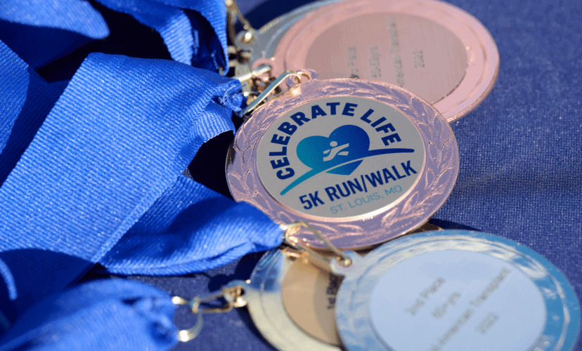 A race medal with a blue ribbon. "Celebrate Life 5k Run/Walk" is printed on the medal.