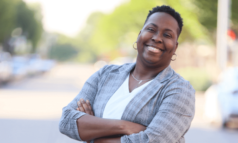 Dr. Brittany Clayborne stands with arms crossed, smiling. She is wearing a grey plaid blazer.