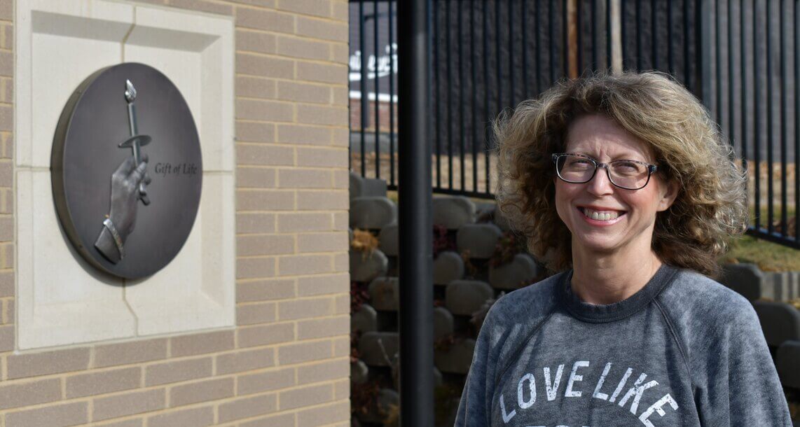 A woman with a grey sweater stands in front of the donor memorial at the Mid-America Transplant Family House