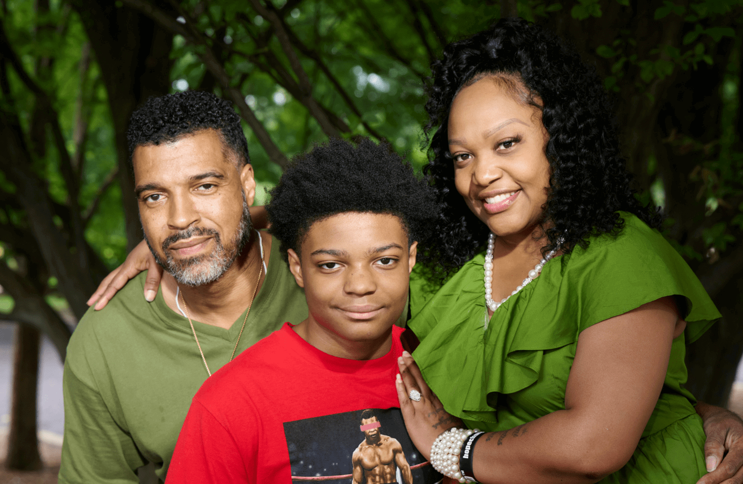 Dee poses with her husband, Robert Jr. They are both wearing green. Their son, Robert III, sits between them.