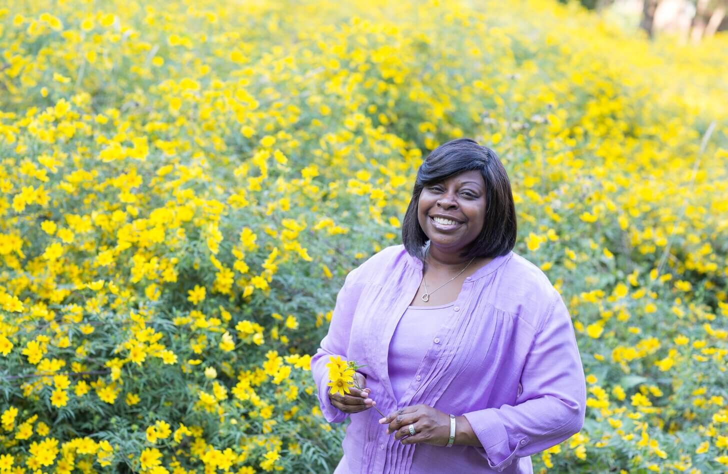 Nikki stands in a field of yellow flowers