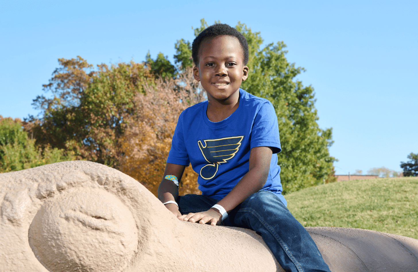 Lakevious, pediatric liver recipient, sitting on a statue in a park
