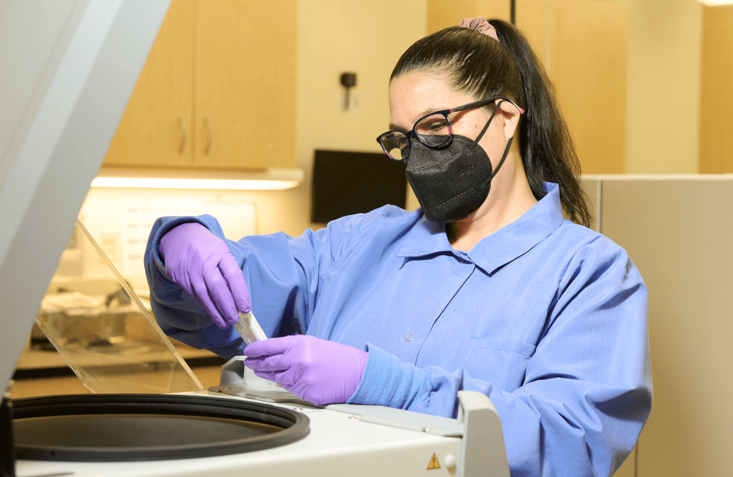 Jennifer M. working in the lab at Mid-America Transplant. She is wearing purple gloves and a black mask.