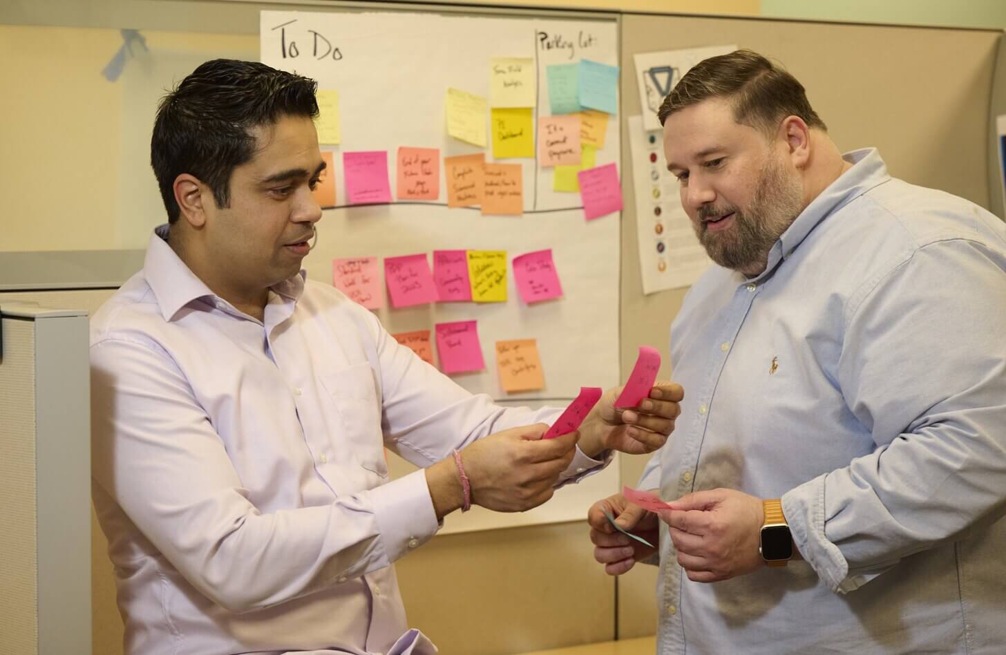 Vikram, a business intelligence employee, works with Louie from the Performance Excellence team to improve processes. Vikram is holding two pink post-it notes.