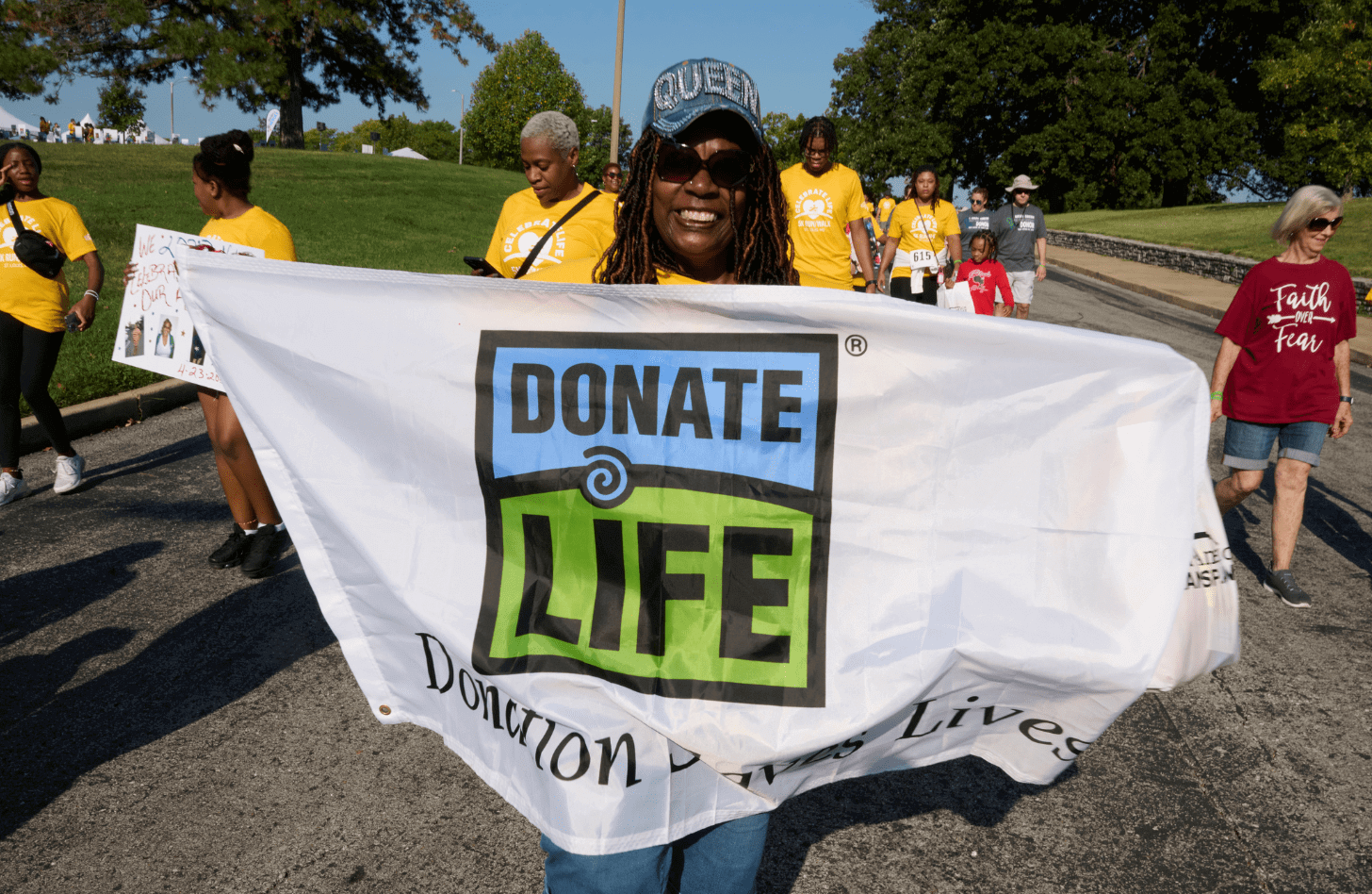 A woman holds up a flag with the Donate Life logo on it. Underneath the logo reads "Donation Saves Lives"
