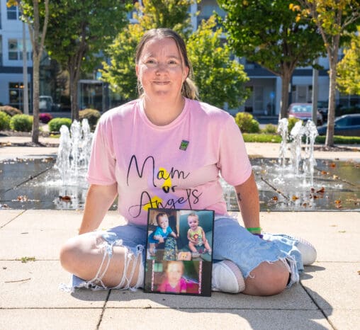 A donor mom sits in front of a fountain with photos of her children